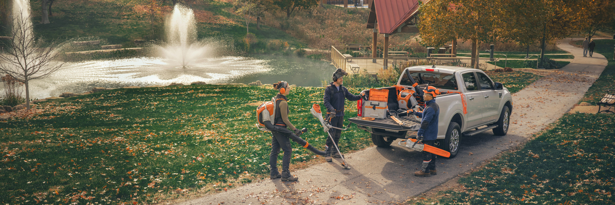  Un gruppo di giardinieri paesaggisti professionisti si trova intorno ai loro veicoli e si prepara al lavoro con gli attrezzi a batteria STIHL.