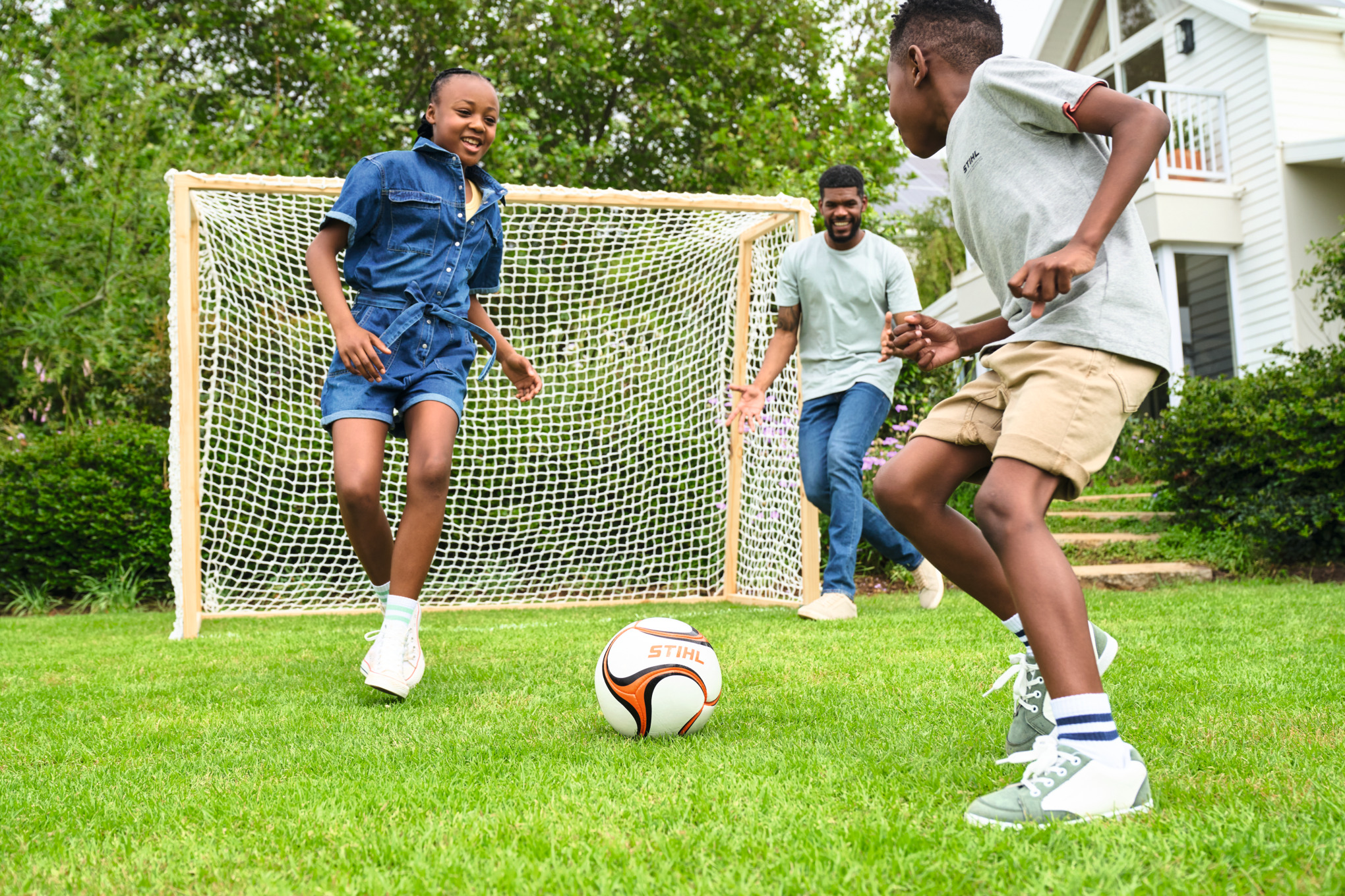 Tre bambini giocano a calcio in giardino con una porta da calcio in legno