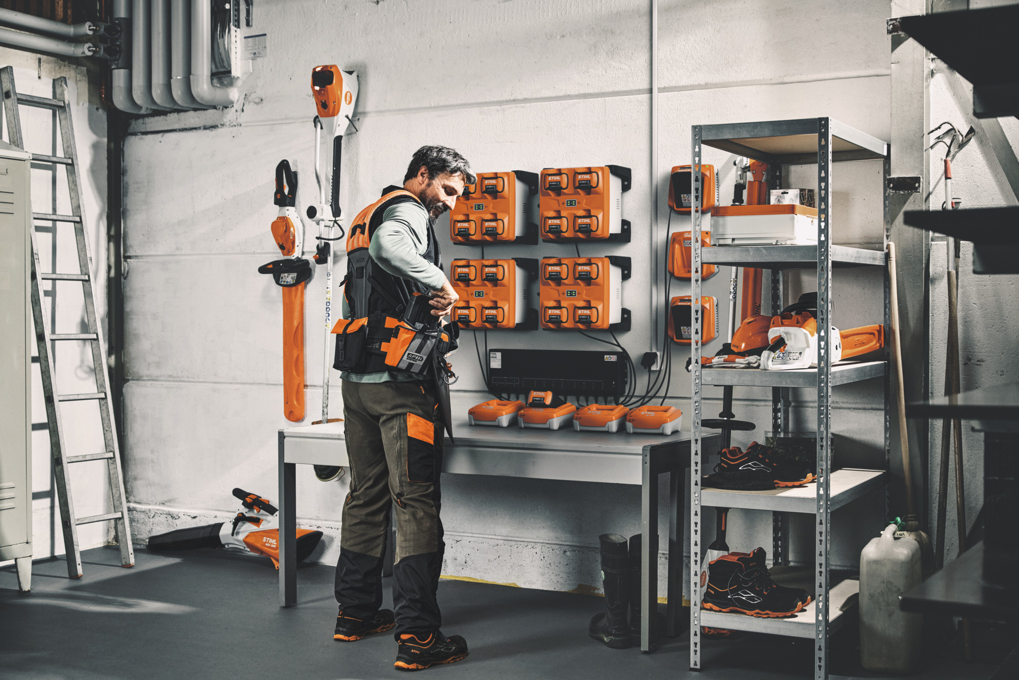 Un uomo in un magazzino con attrezzi e batterie STIHL indossa il sistema di imbracatura modulare STIHL ADVANCE X-Flex 