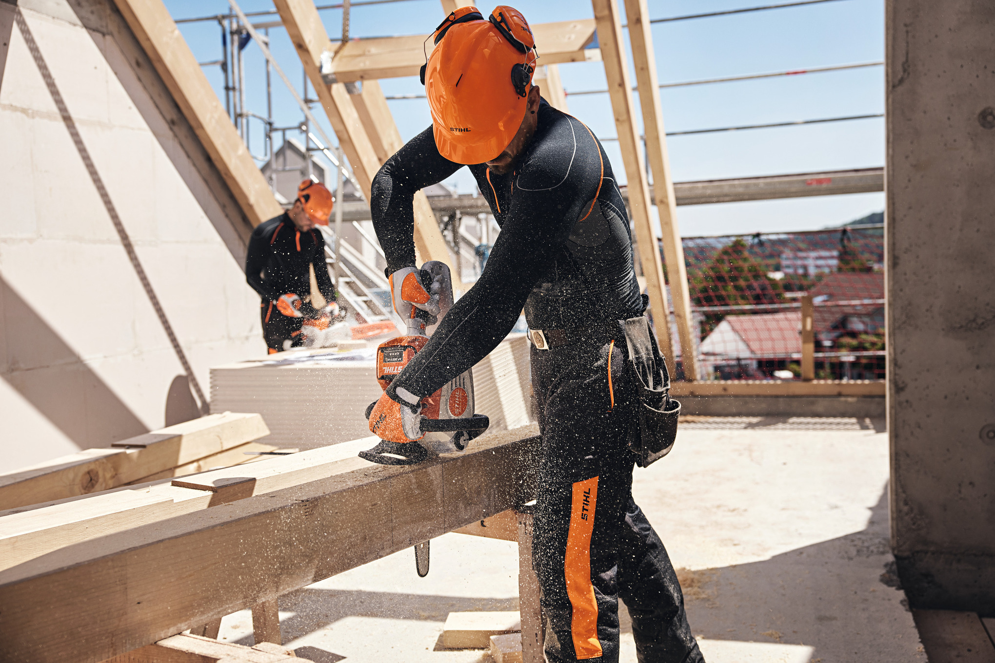 Professionista che sega una trave di legno in una capriata utilizzando una motosega a batteria STIHL, sullo sfondo un altro operaio maneggia un'altra motosega a batteria
