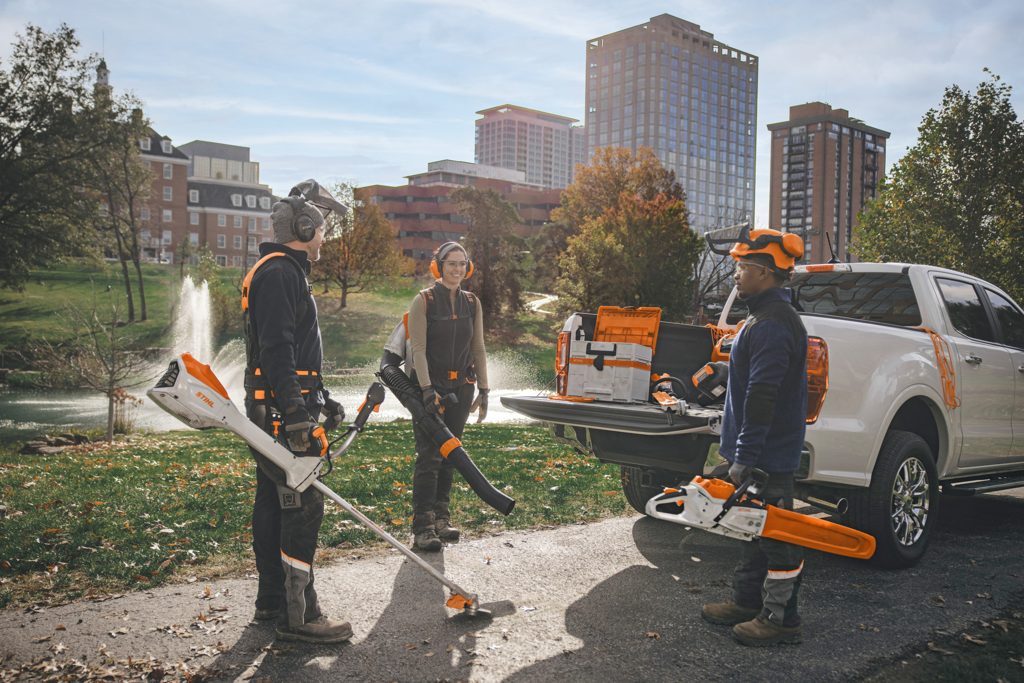 Un gruppo di paesaggisti professionisti, in piedi attorno ai propri veicoli, si prepara a lavorare con gli utensili a batteria STIHL. 