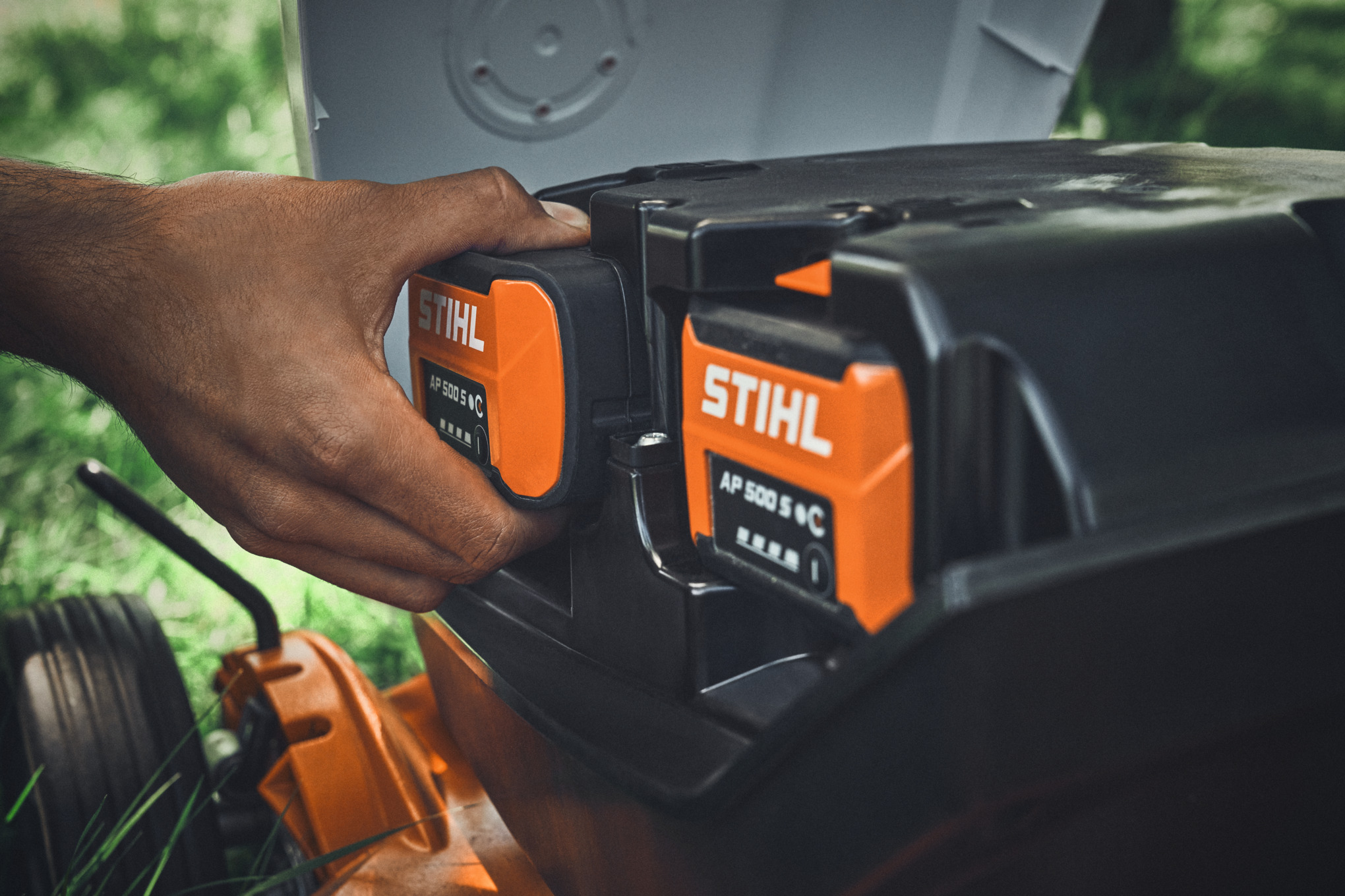 Una persona inserisce una batteria STIHL AP 500 S in un tosaerba a batteria STIHL