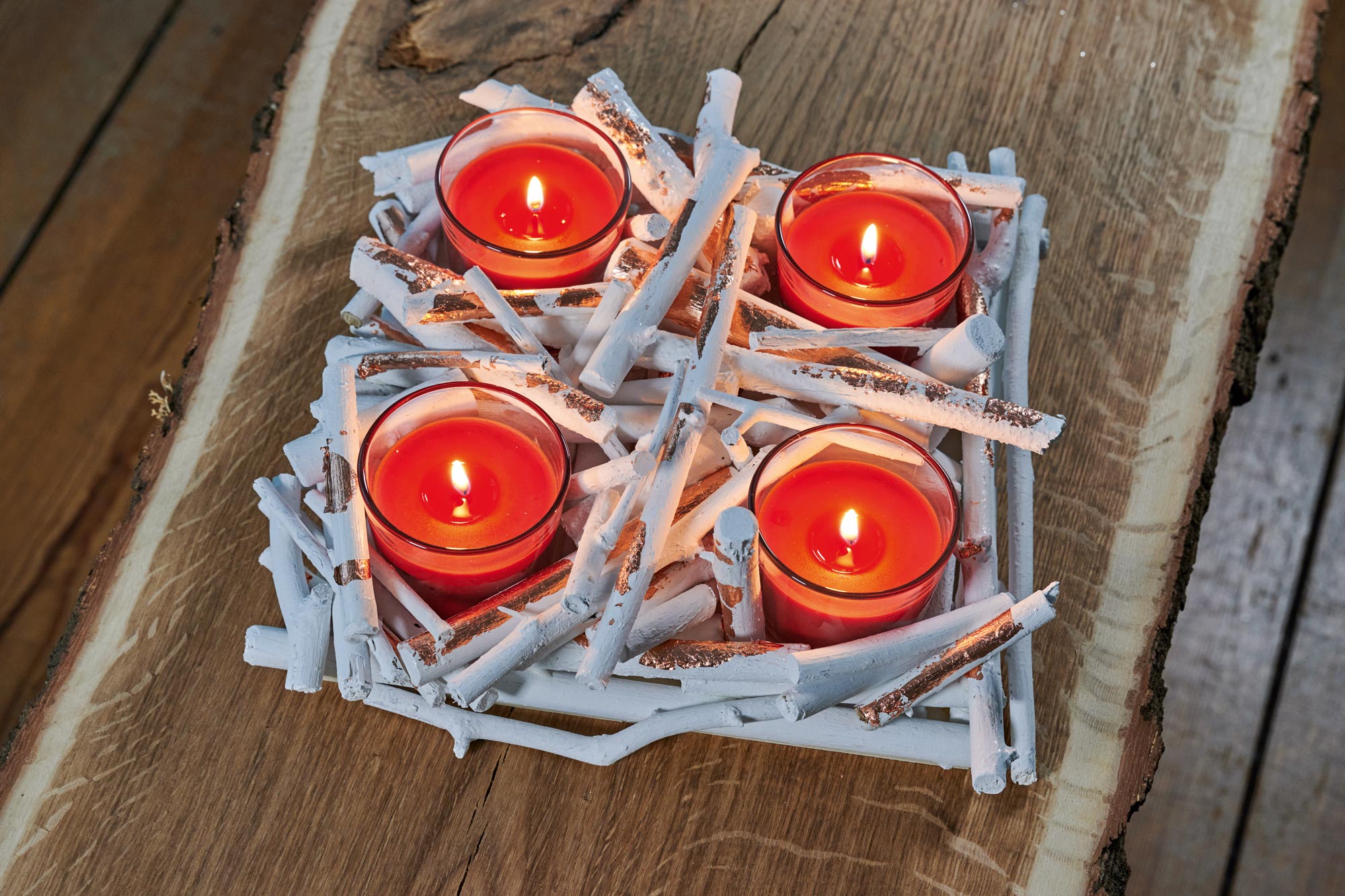 Quattro tealight rosse bruciano in una corona d'Avvento fai da te fatta di rami