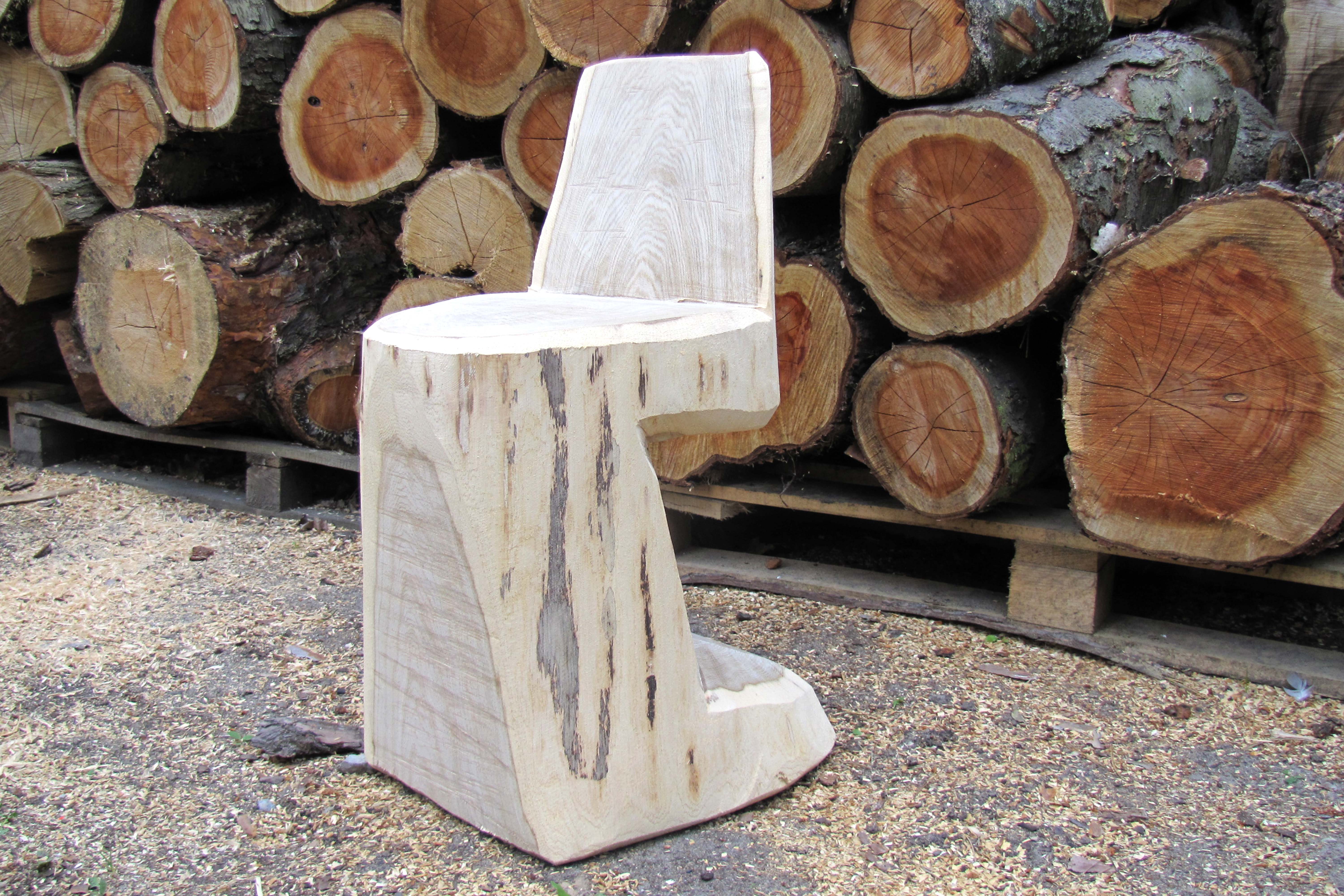 Sedia di legno fai da te davanti a una catasta di tronchi