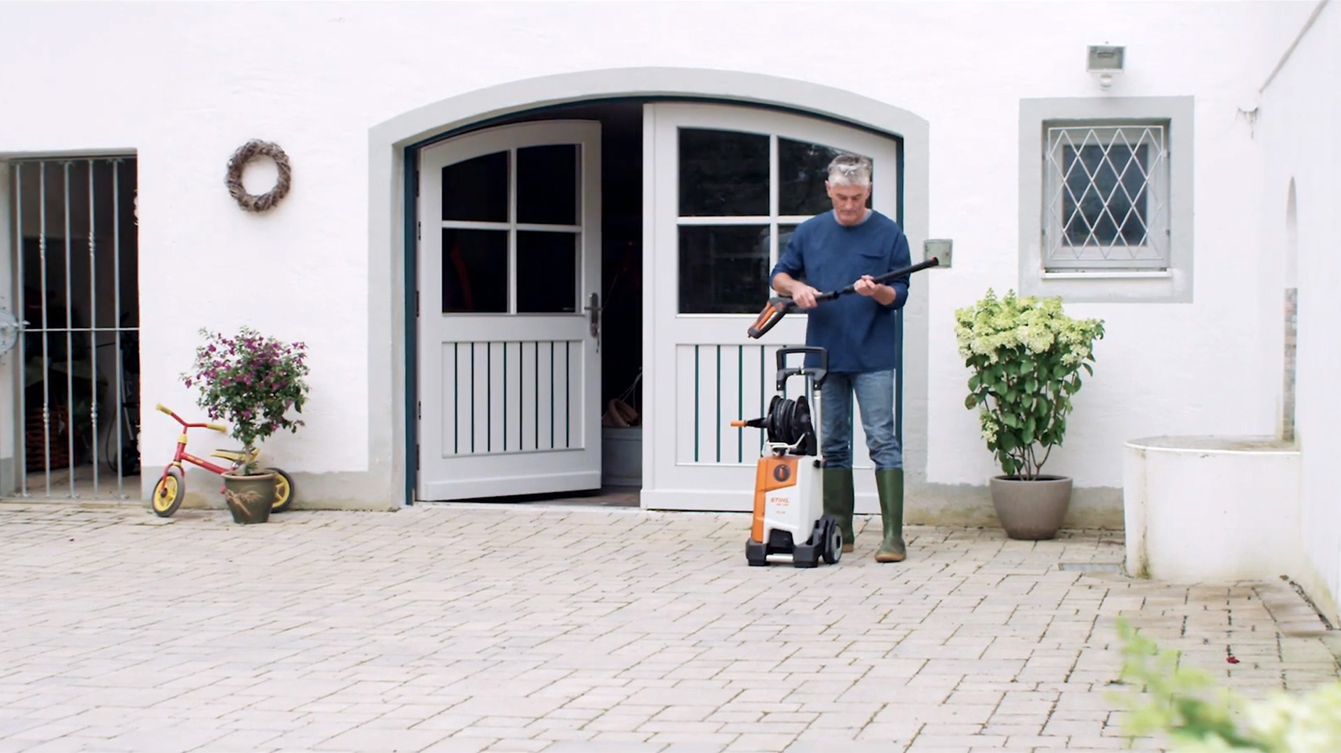 Uomo in piedi davanti a una casa bianca che prepara l'idropulitrice STIHL per pulire la facciata