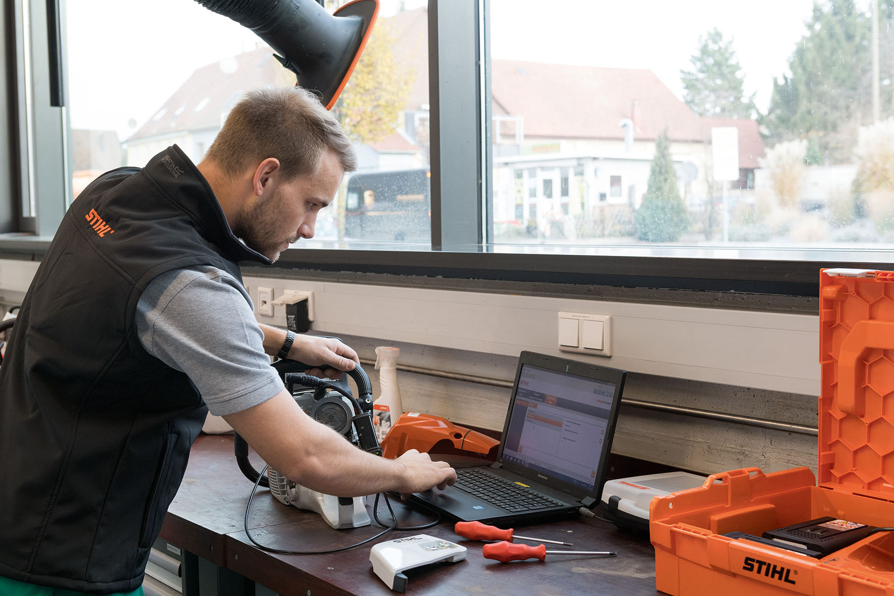 Un uomo guarda un laptop in un'officina. Accanto, una motosega STIHL.