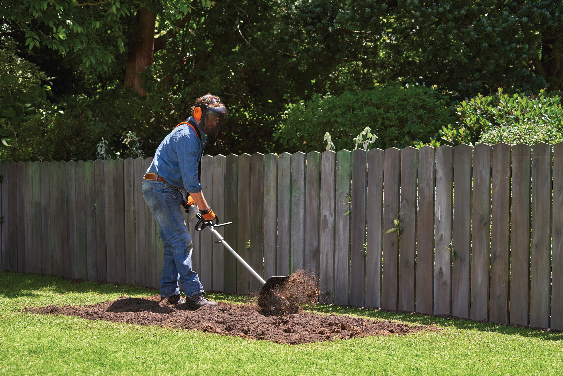 Persona munita di dispositivi di protezione individuale che scava una superficie del giardino utilizzando lo STIHL KombiSystem con fresa per terreno allo scopo di realizzare un'aiuola