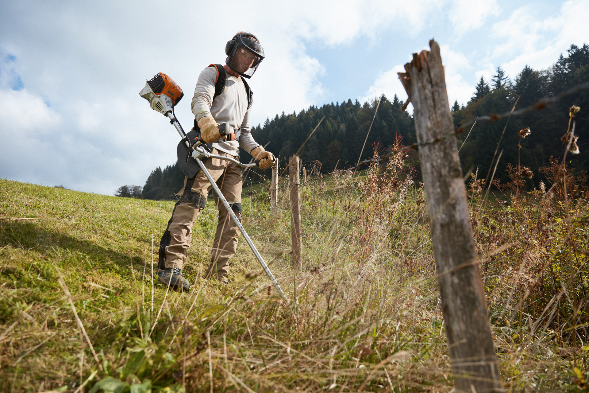 Uomo con dispositivi di protezione individuale che falcia il prato in pendenza con un decespugliatore a benzina STIHL FS 91