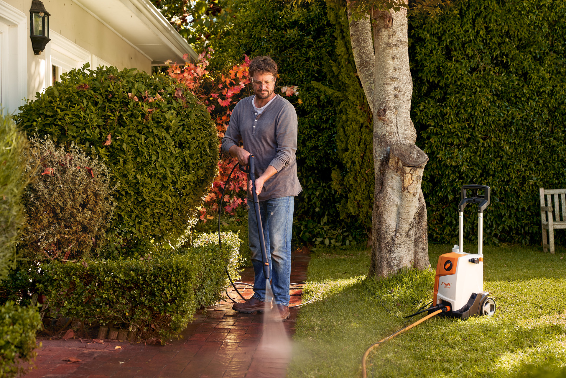 Uomo che pulisce un pavimento in pietra esterno antistante la casa, utilizzando l'idropulitrice STIHL RE 110.