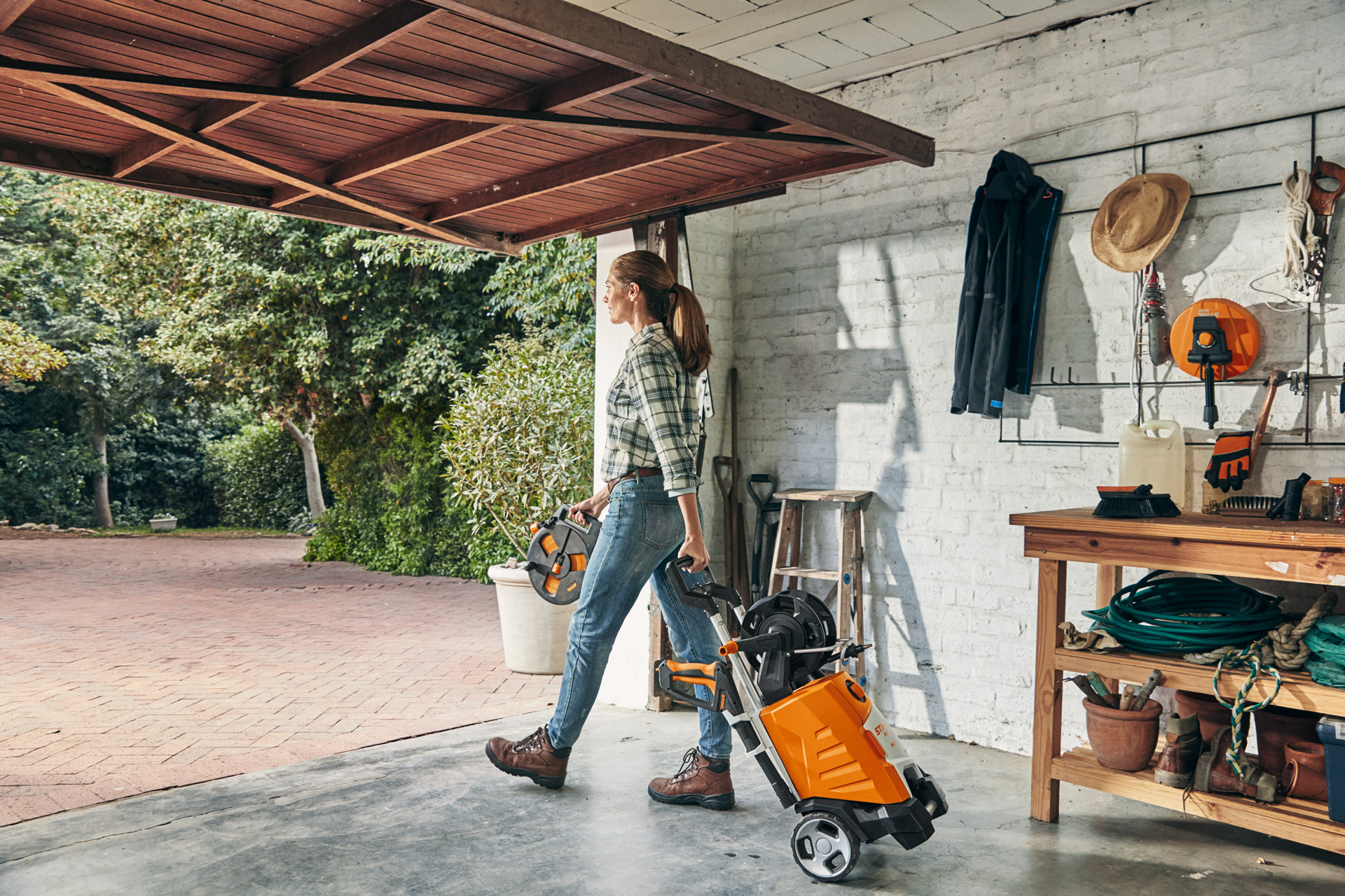 Una donna esce da un garage con l'idropulitrice ad alta pressione STIHL RE 130 PLUS per utilizzarla.