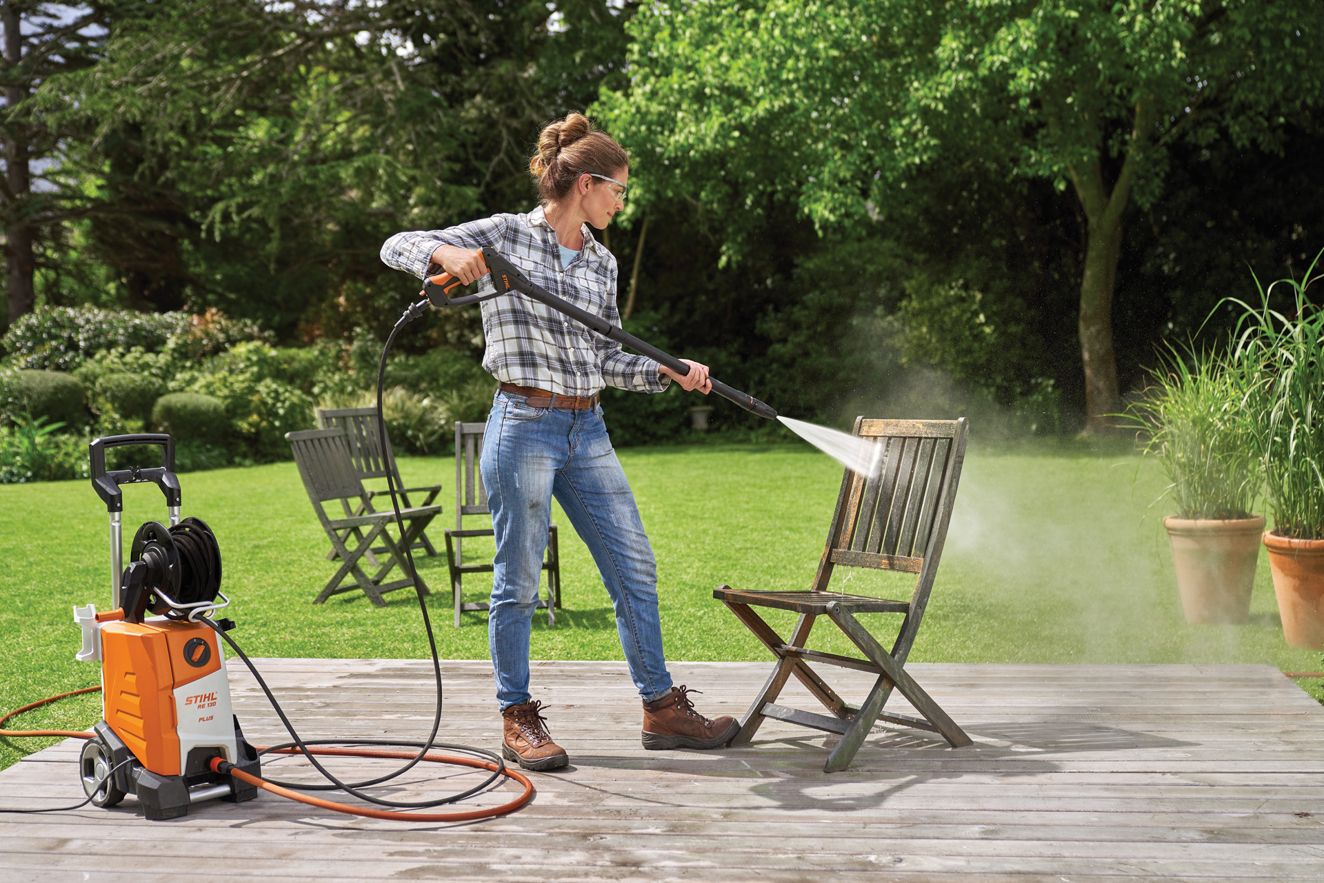 Donna che pulisce un mobile da giardino in legno con un'idropulitrice STIHL RE 130 plus sul terrazzo