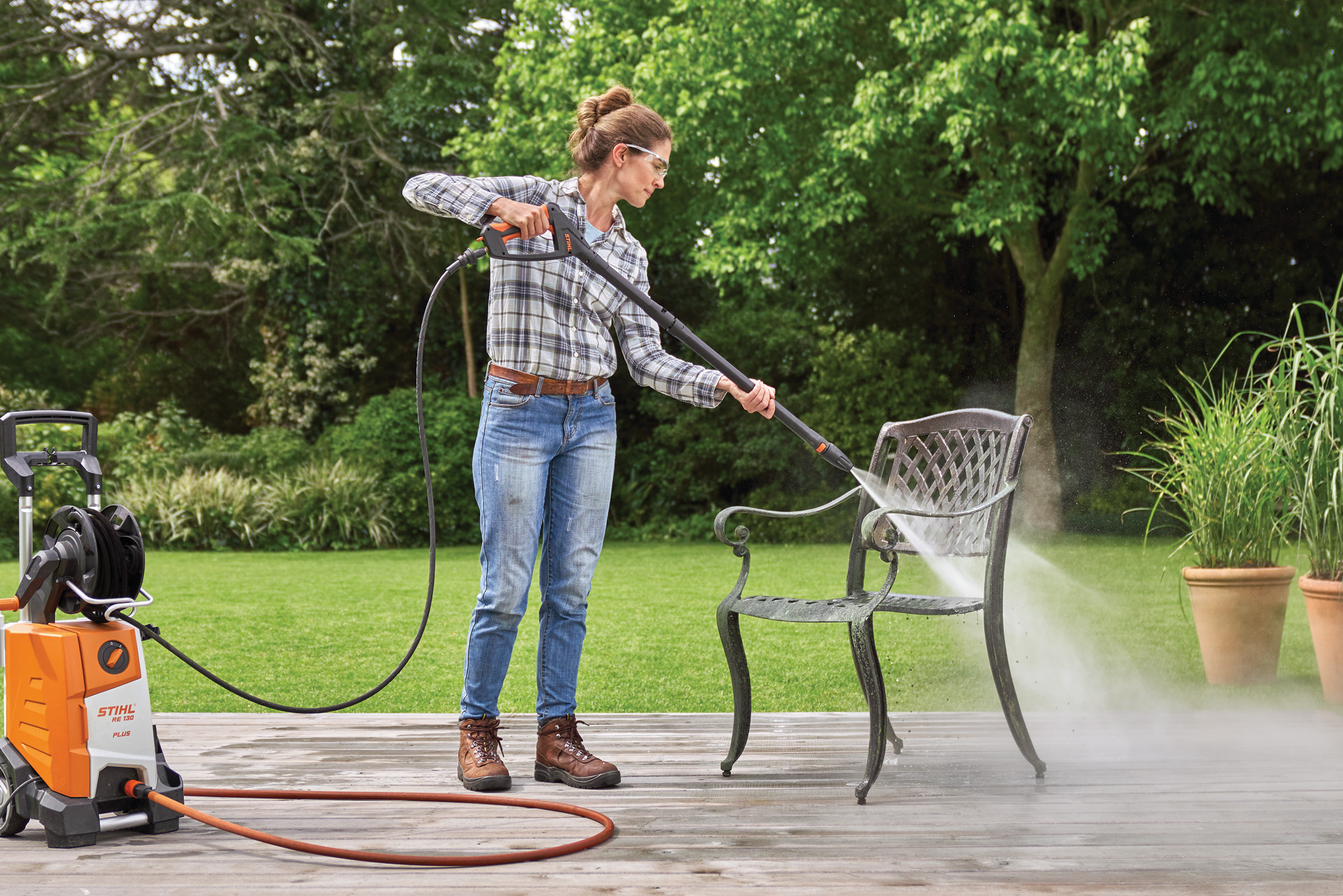 Donna che pulisce un mobile da esterno in metallo con l'idropulitrice STIHL RE 130 plus sul terrazzo