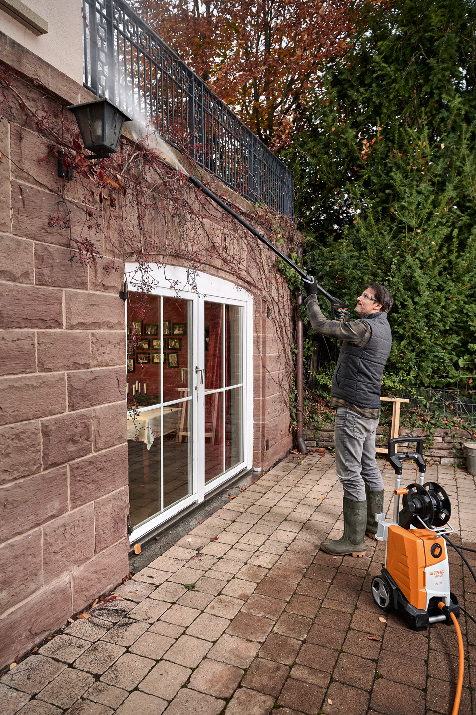 Uomo in piedi sulla terrazza che pulisce la facciata con un'idropulitrice STIHL