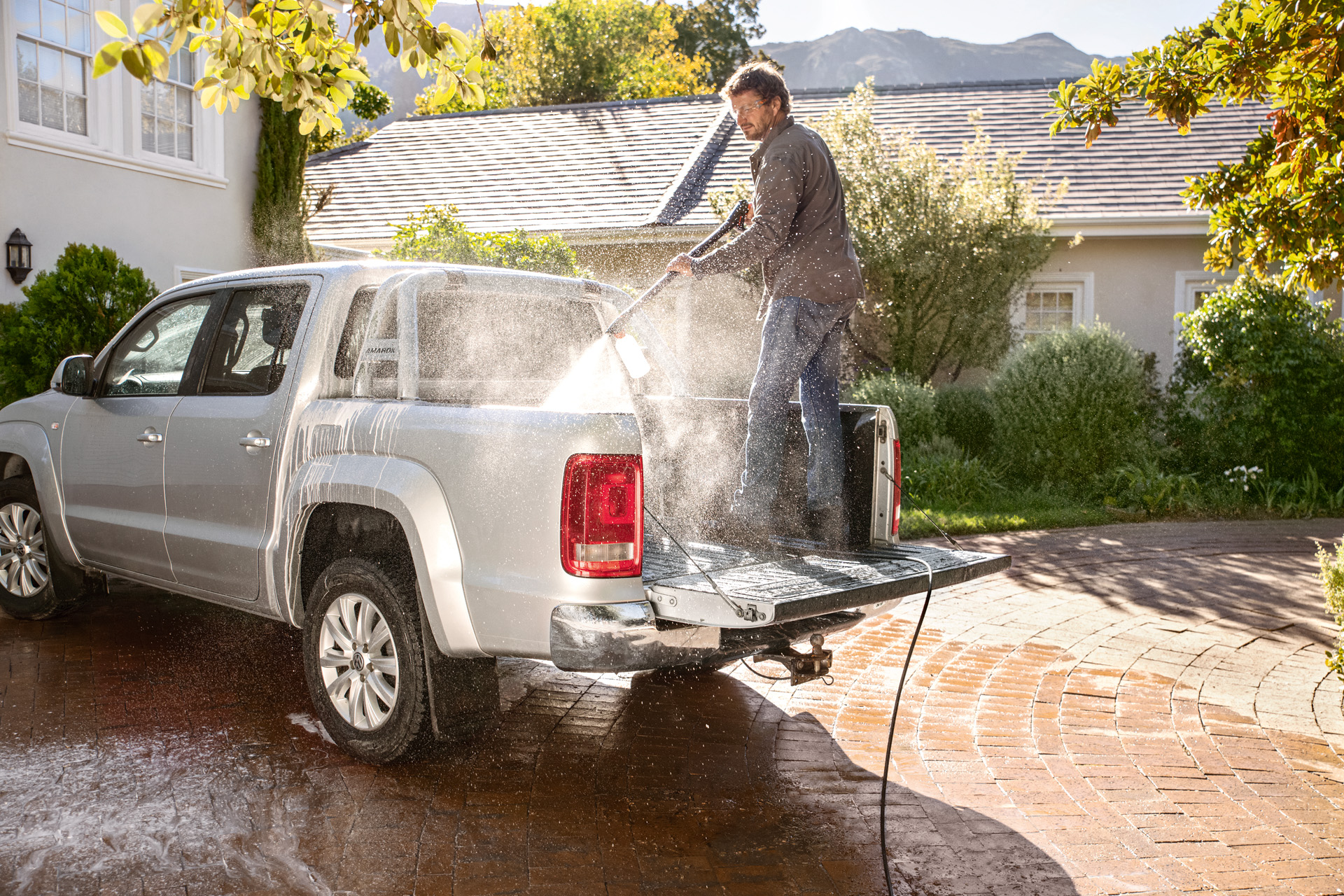 Uomo in piedi sulla superficie di carico di un pick-up che lava l'auto con l'idropulitrice