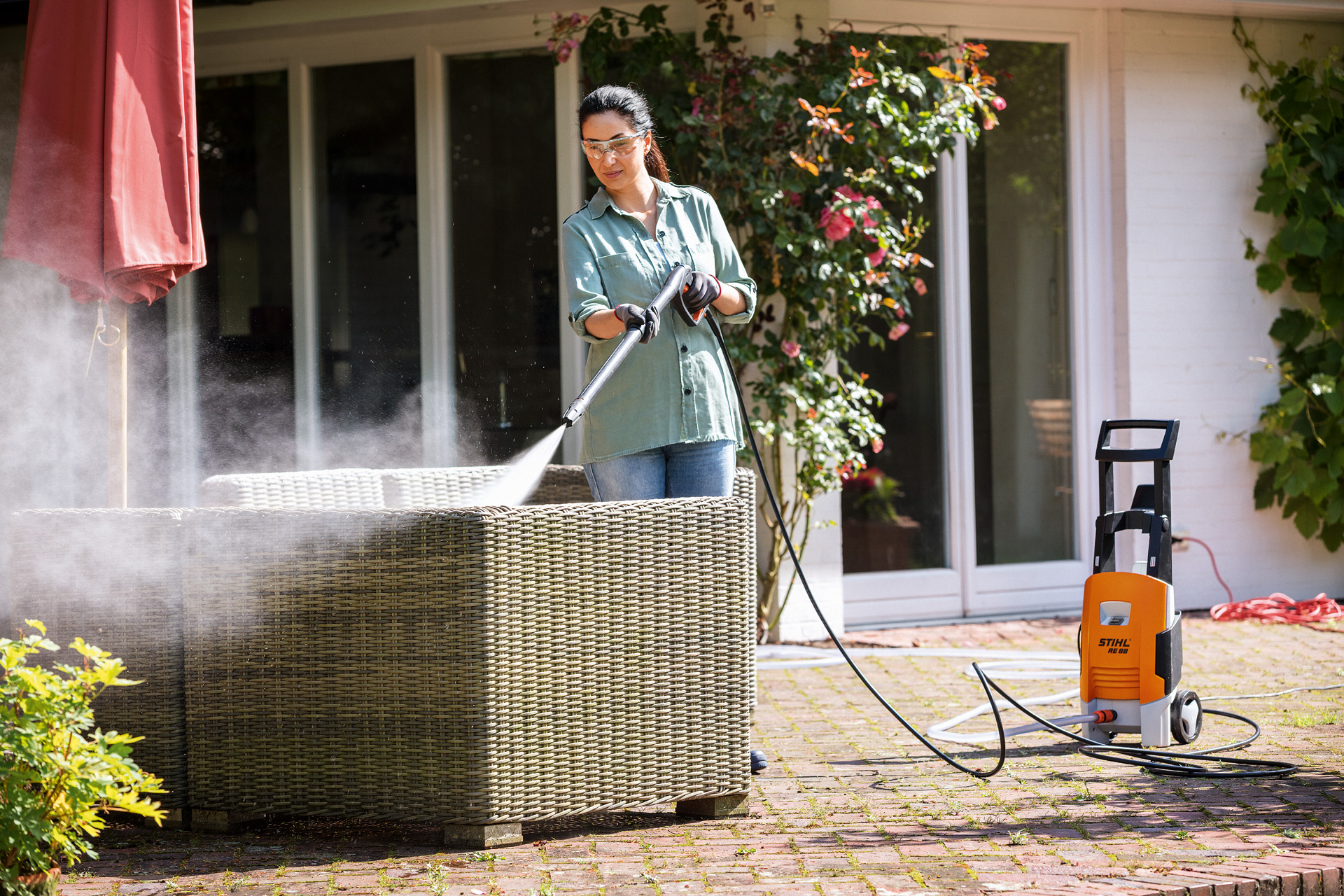 Donna con occhiali di protezione che pulisce i propri mobili da giardino con l'idropulitrice STIHL RE 88 sul terrazzo