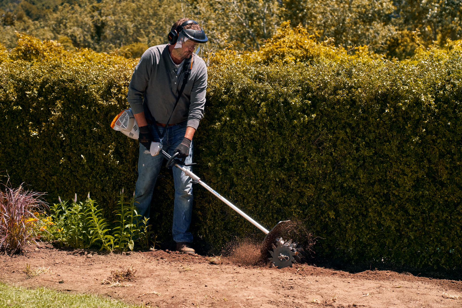 Uomo munito di visiera di protezione che lavora in un'aiuola con lo STIHL Kombimotor KM 56 RC-E