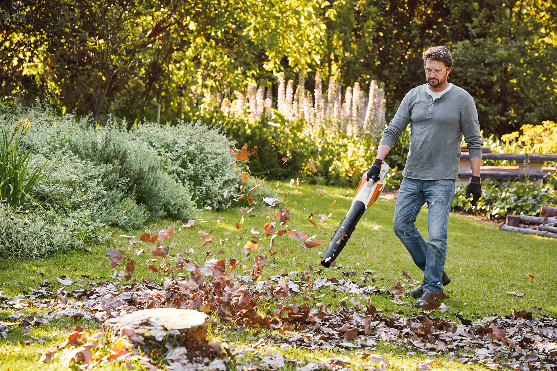 Uomo con occhiali protettivi rimuove le foglie nel suo giardino con il soffiatore a batteria STIHL BGA 57