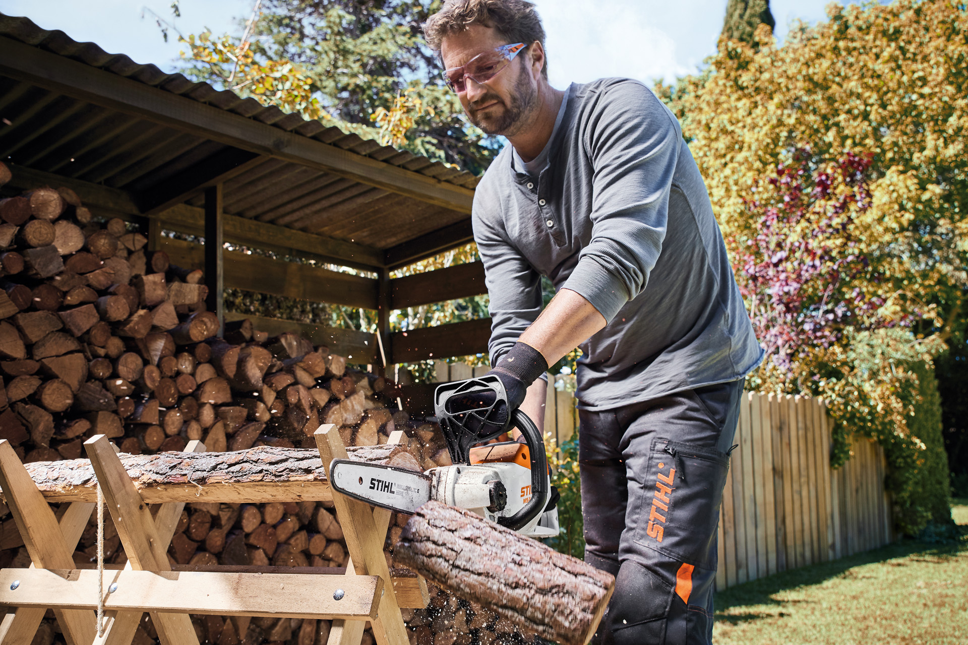 Uomo con occhiali di protezione sega un tronco su un cavalletto con una motosega a batteria STIHL MSA 140 C-B