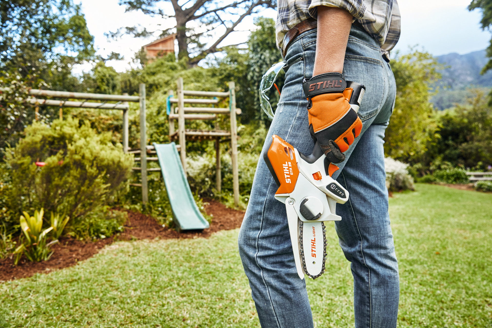 Persona munita di potatore senza fili GTA 26 STIHL all'interno di un giardino davanti a uno scivolo