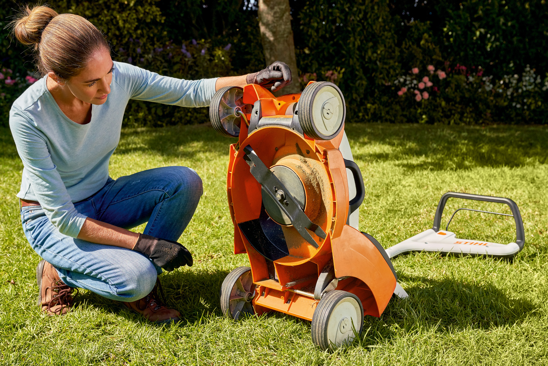 Donna in giardino che guarda sotto il suo tosaerba a batteria STIHL RMA 339C 