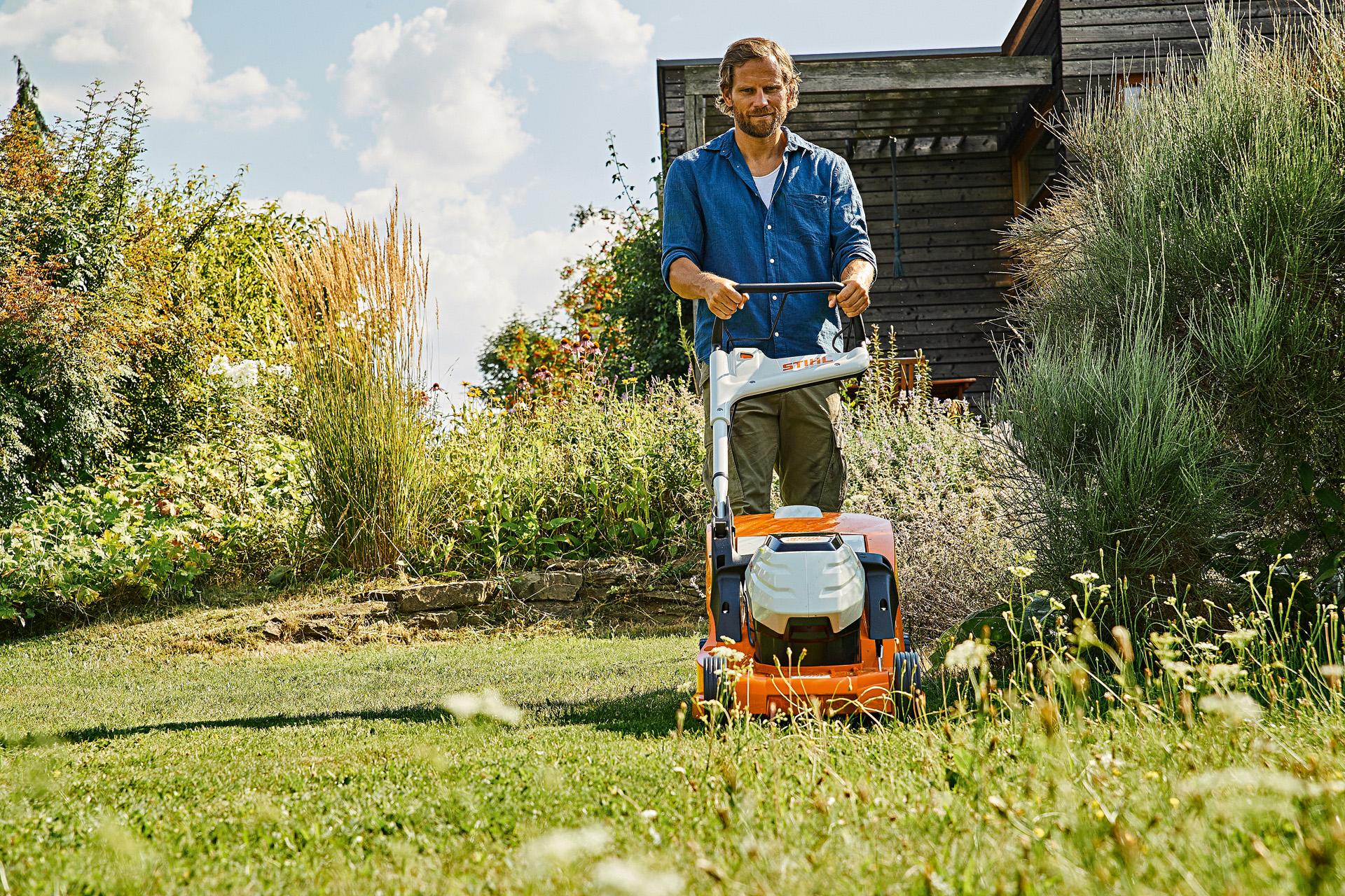 Uomo che utilizza il tosaerba a batteria STIHL RMA 448 P-C in un giardino per la cura del prato in estate