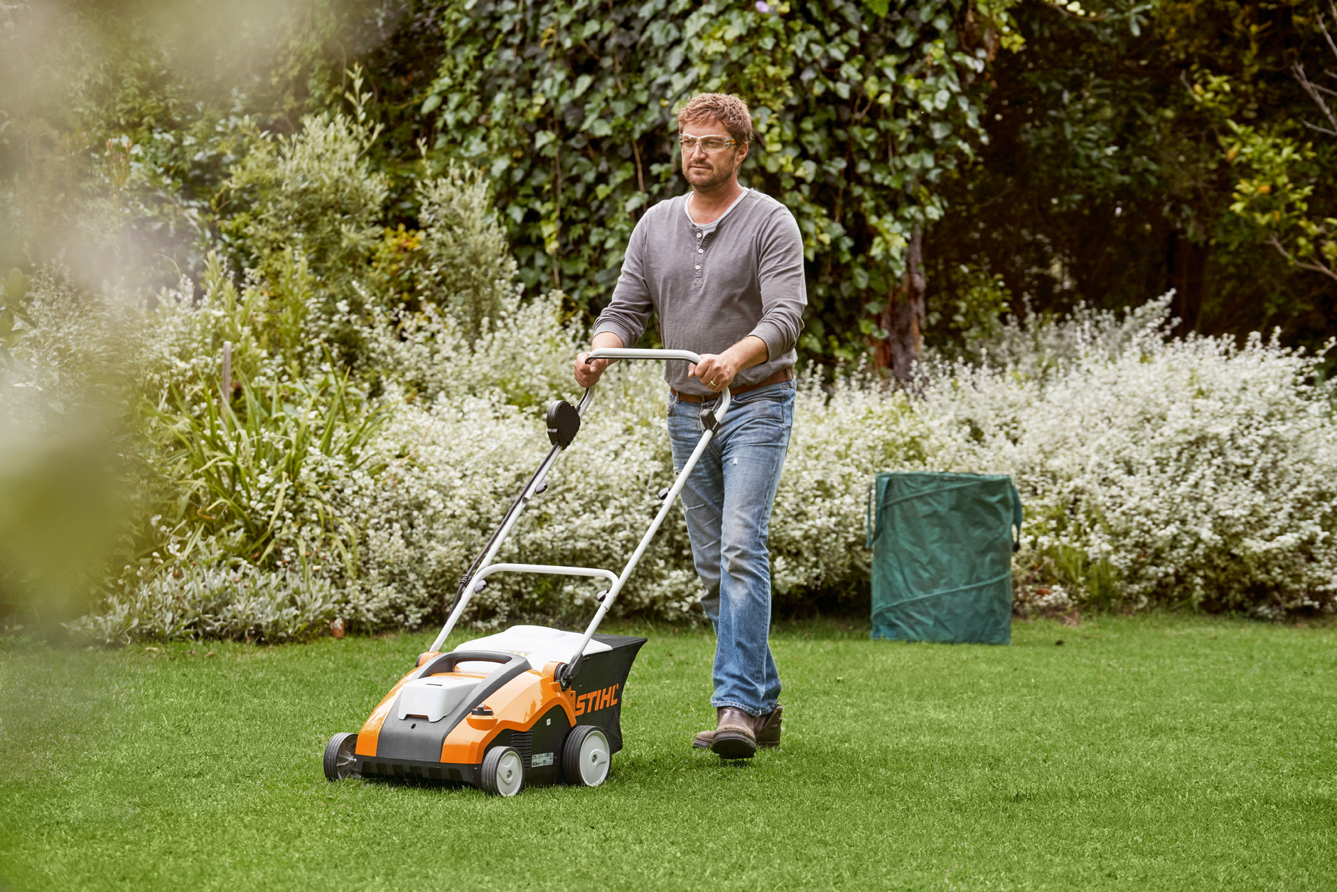 Uomo arieggia superficialmente il prato verde con un arieggiatore a batteria STIHL RLA 240