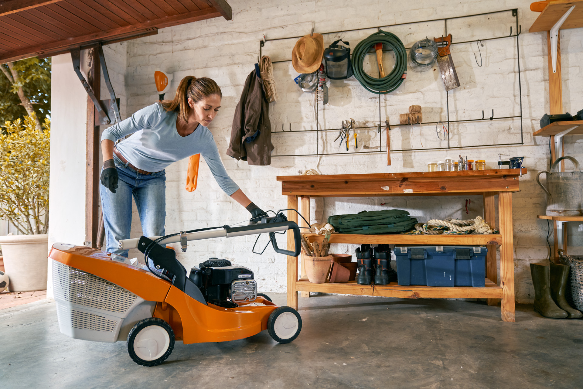 Donna che prepara il tosaerba a benzina STIHL RM 448 TC per l'inverno in garage e lo ripone