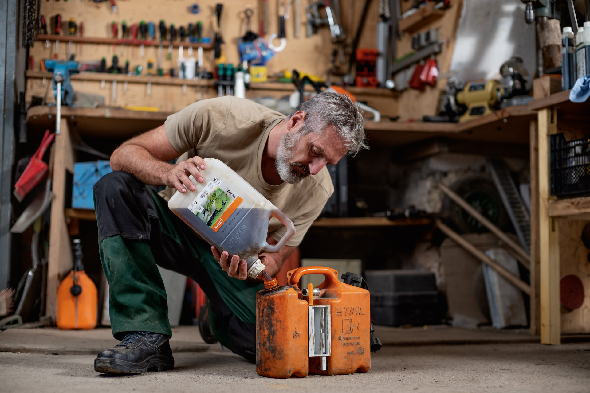 Uomo inginocchiato sul pavimento di un'officina che versa il carburante STIHL in una tanica arancione