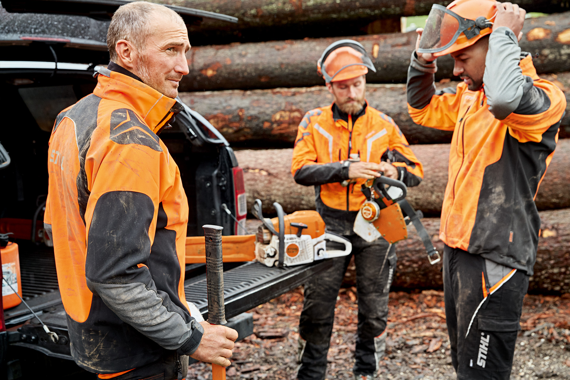 Tre lavoratori forestali con dispositivi di protezione individuale davanti ad un tronco nel bosco.