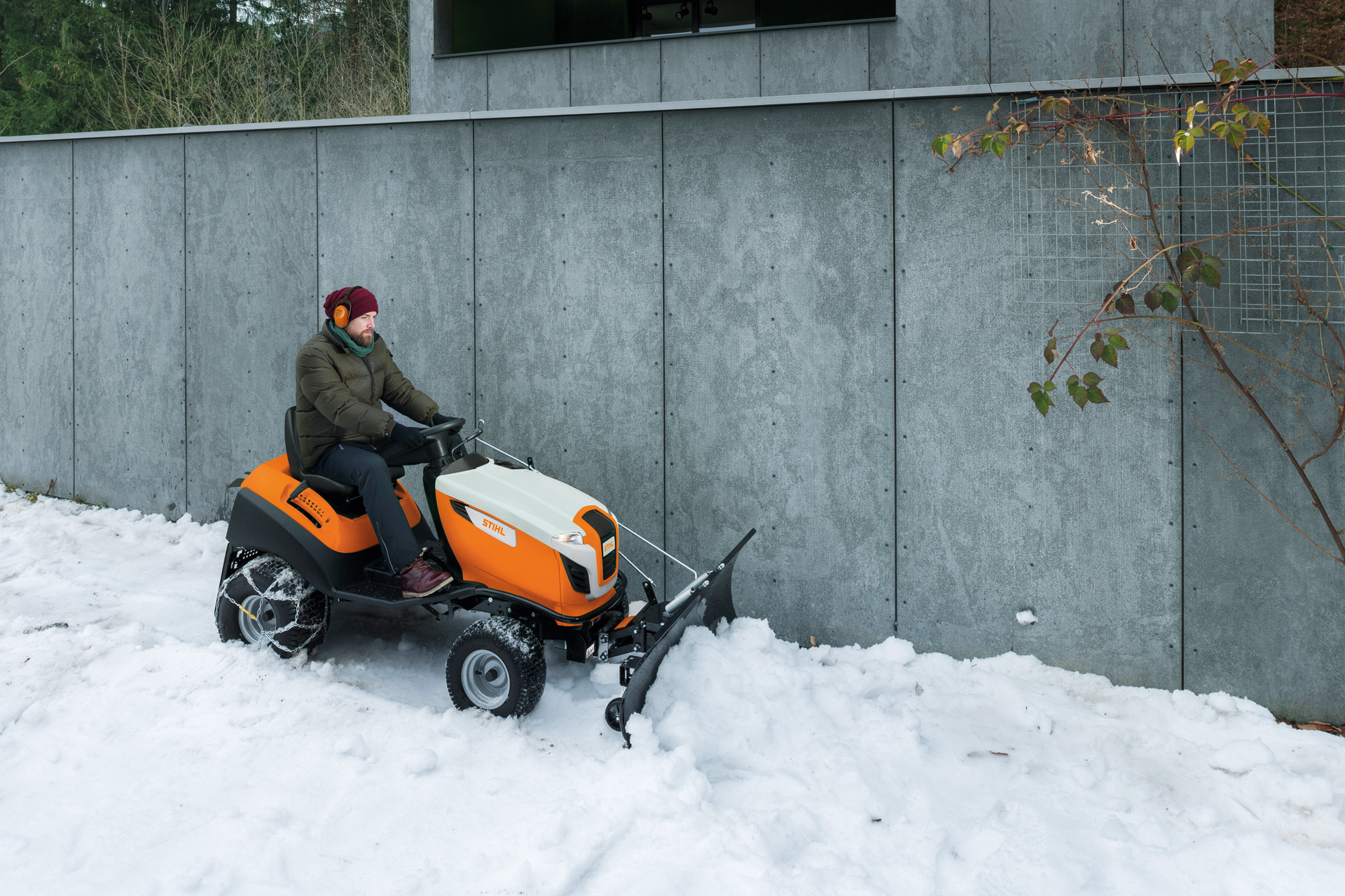 Uomo che sgombra la neve davanti a un muro su un trattorino da giardino con pala da neve 