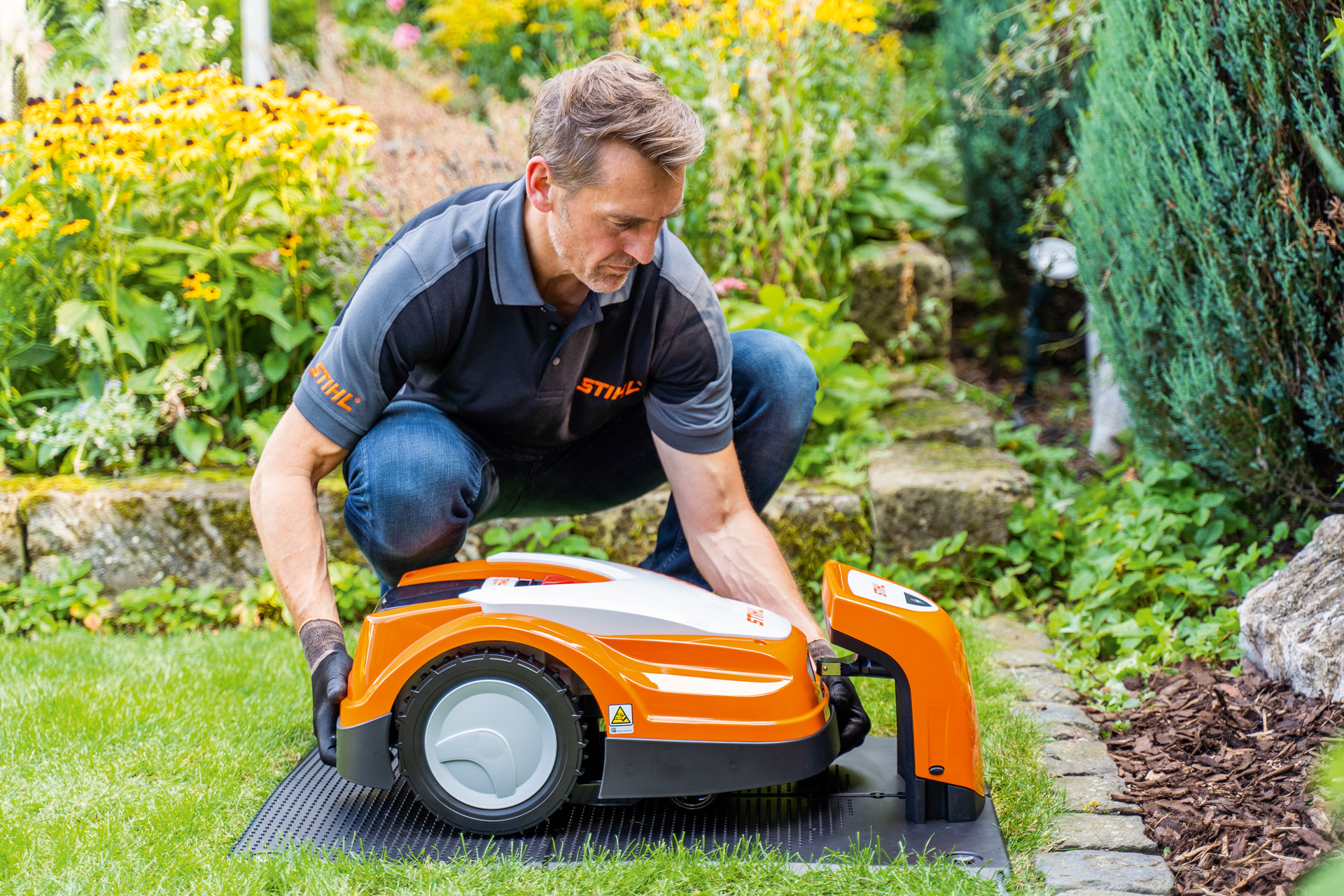 Un rivenditore STIHL mette un robot tosaerba STIHL iMOW nell'apposita stazione di ricarica in un giardino