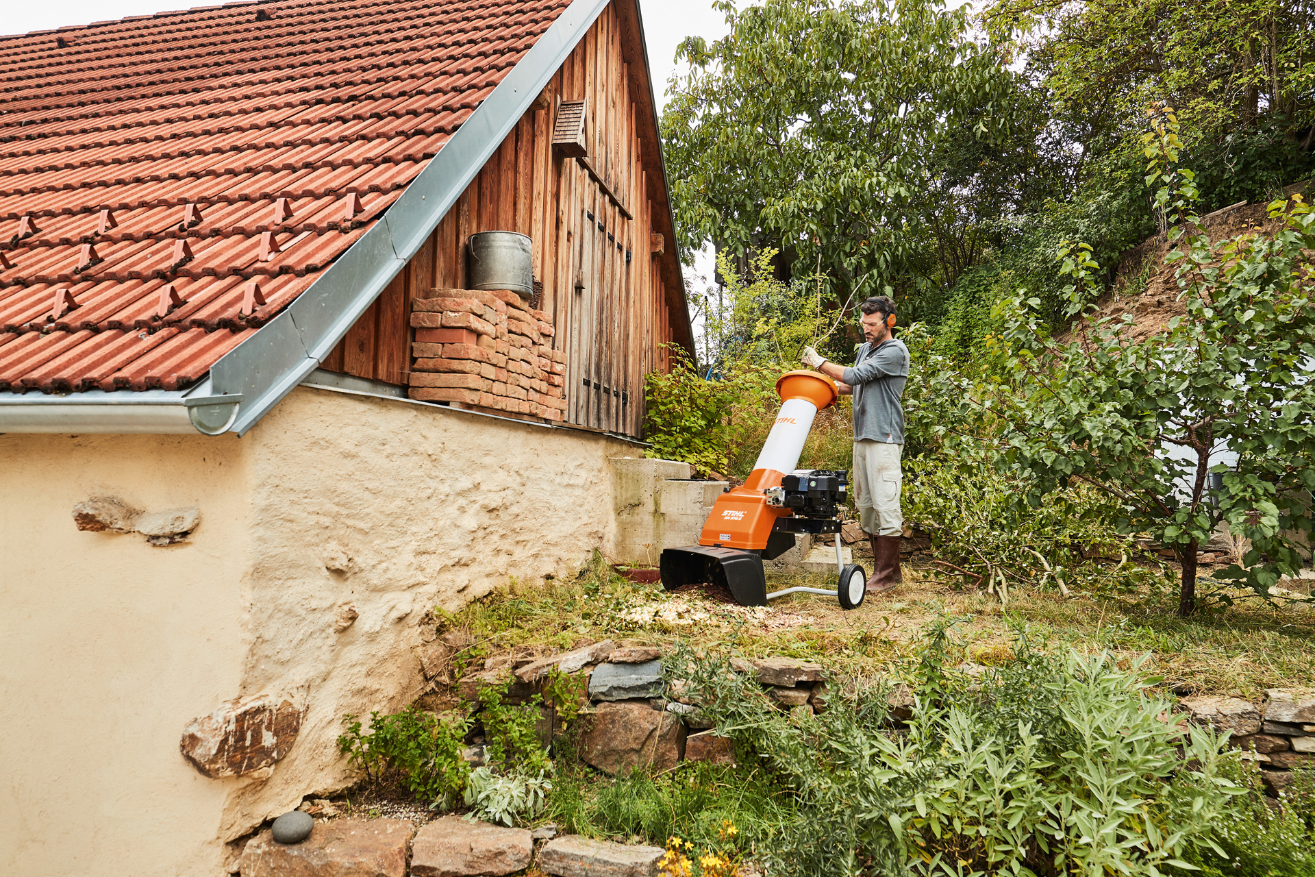 Uomo che utilizza un biotrituratore a benzina STIHL tra gli alberi e i cespugli davanti a un'abitazione