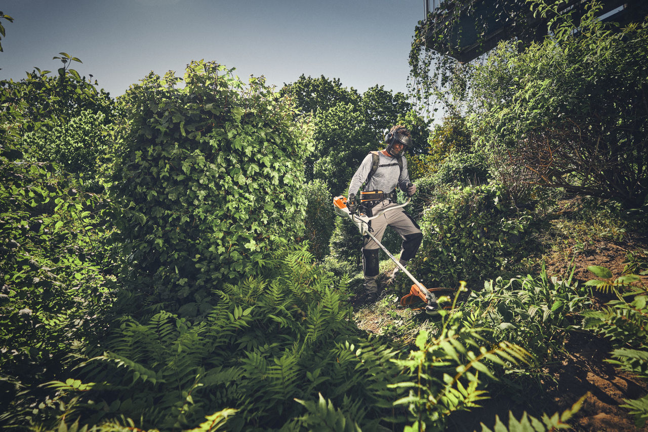 Una persona in equipaggiamento protettivo taglia il sottobosco che cresce selvaggio con un decespugliatore STIHL