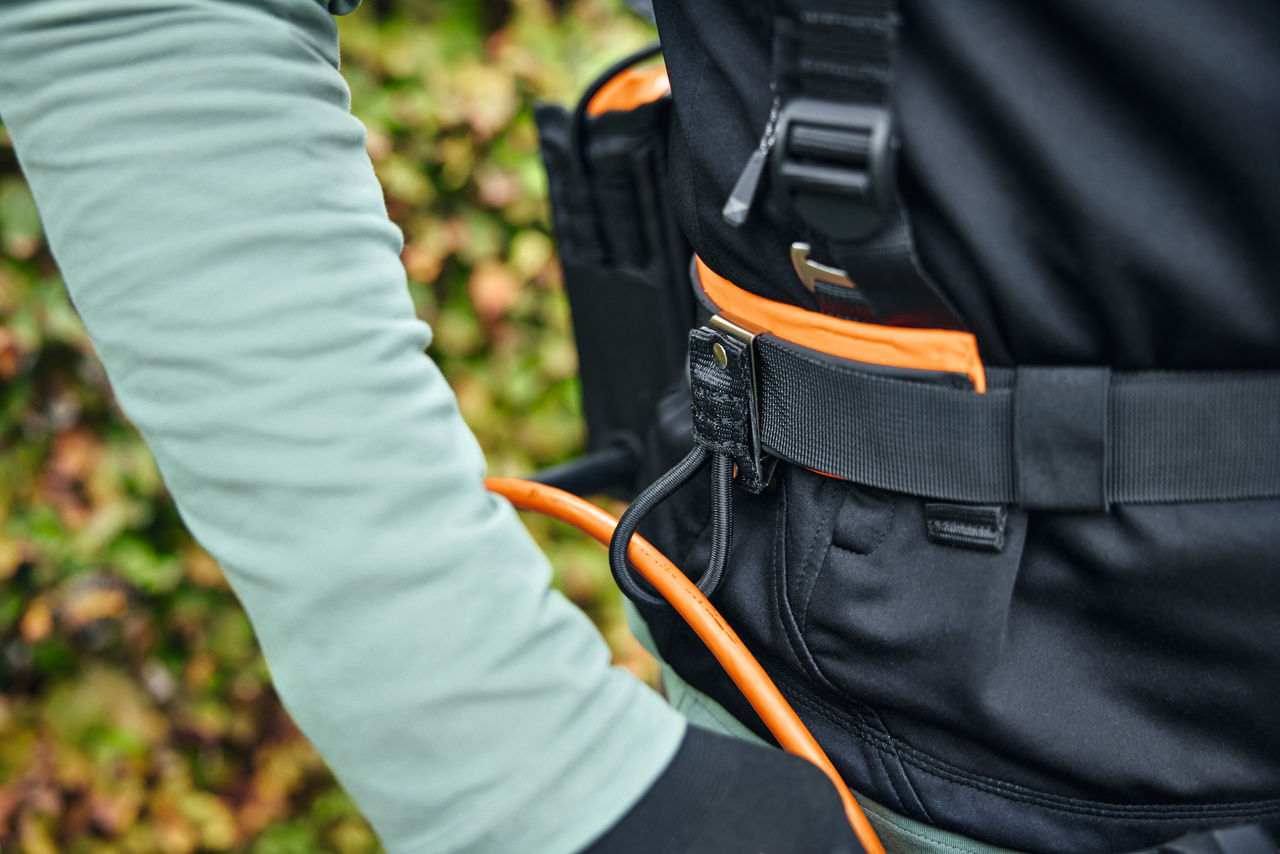 Una persona indossa il sistema di imbracatura modulare STIHL ADVANCE X-Flex con una borsa per batteria con cavo di collegamento e guida per i cavi