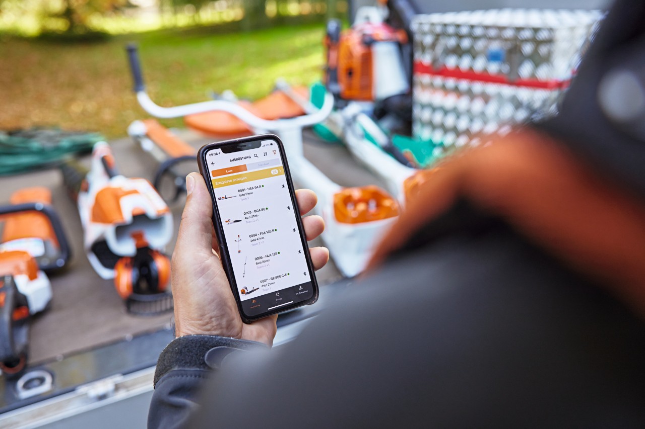 Qualcuno si trova davanti al vano di carico di un veicolo cassonato su cui sono collocate diverse attrezzature STIHL. La persona tiene in mano uno smartphone sul quale è aperta l'app STIHL Connected. 