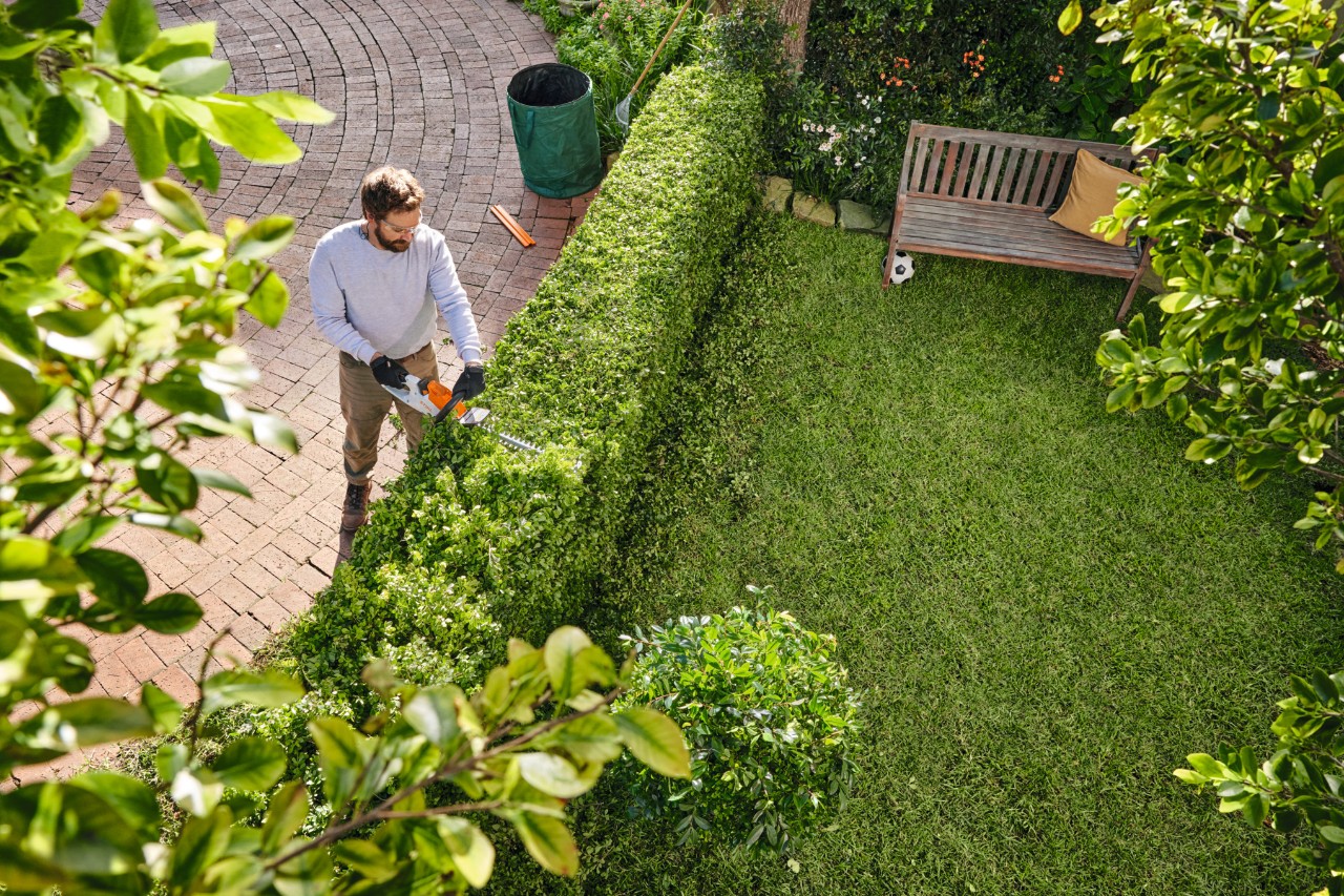 Un uomo taglia la siepe del suo giardino con un tosasiepi STIHL HSA 40