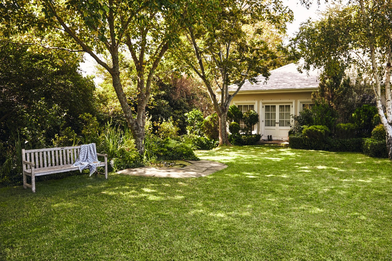 Casetta con giardino, in primo piano una panca da giardino su prato verde