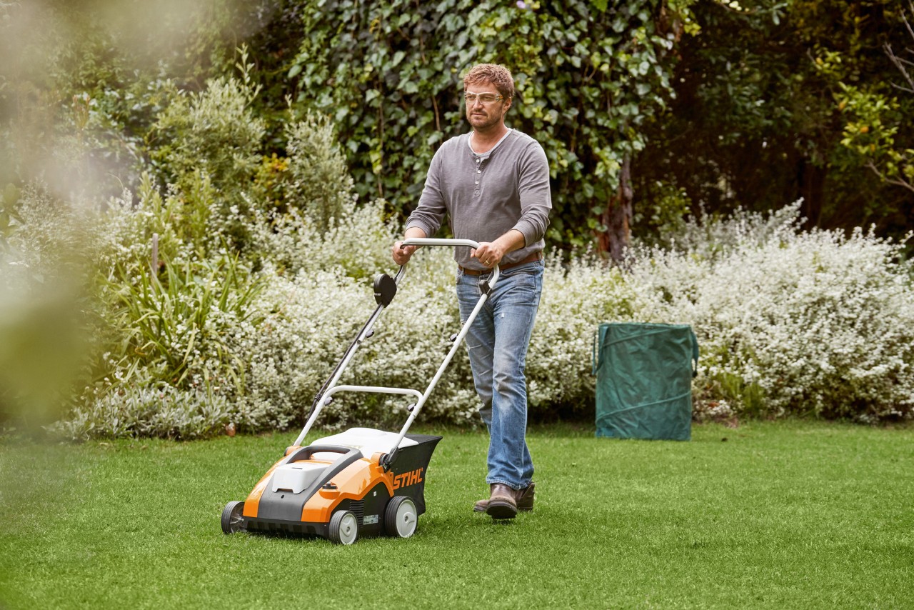 Uomo scarifica il prato verde con un arieggiatore a batteria STIHL RLA 240