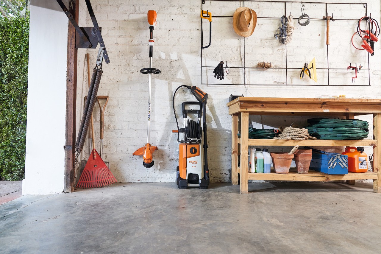 L'idropulitrice ad alta pressione STIHL RE 130 plus e un decespugliatore STIHL sono immagazzinati in garage accanto agli utensili da giardino.
