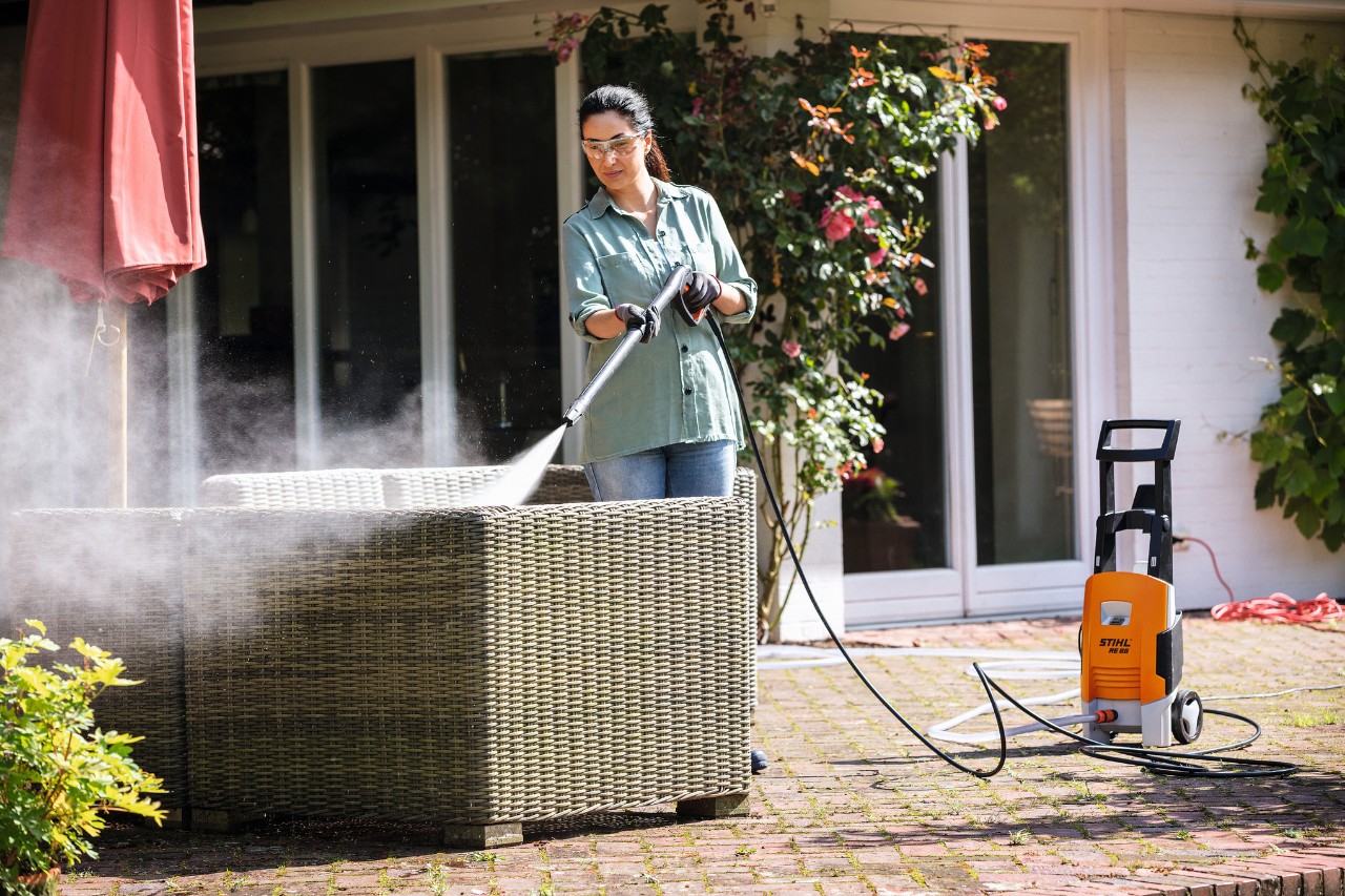 Donna con occhiali di protezione che pulisce i propri mobili da giardino con l'idropulitrice STIHL RE 88 sul terrazzo