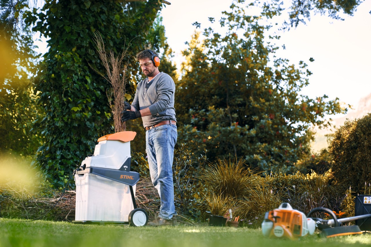 Uomo che utilizza un biotrituratore a benzina STIHL tra gli alberi e i gli arbusti davanti a un'abitazione