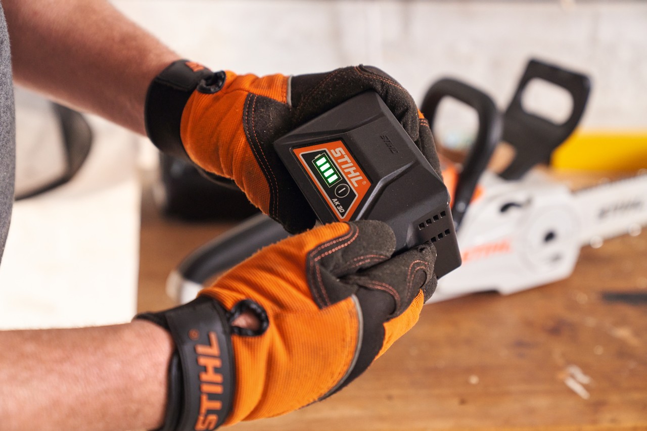 Una persona che indossa i guanti di protezione STIHL tiene in mano una batteria agli ioni di litio STIHL