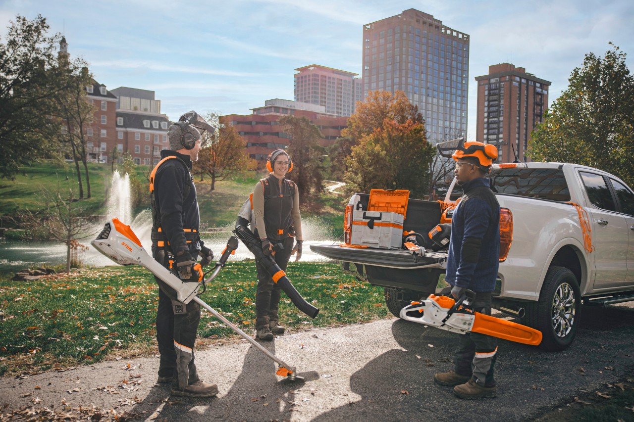 Un gruppo di paesaggisti professionisti in piedi intorno ai propri veicoli mentre si preparano a lavorare con gli utensili a batteria STIHL.