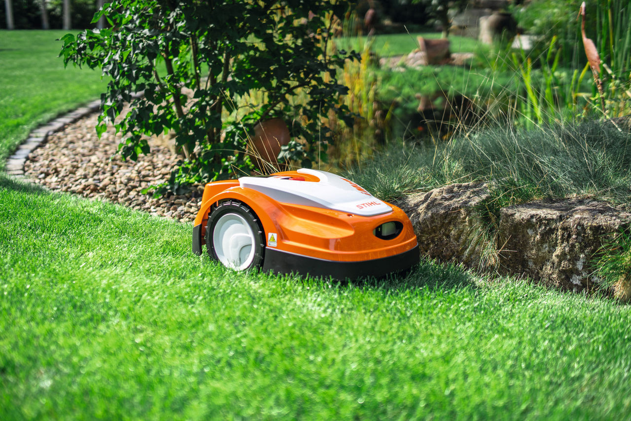 STIHL iMOW RMI 422 mäht auf einer Wiese im Garten am Rand von einer kleinen Steinmauer.