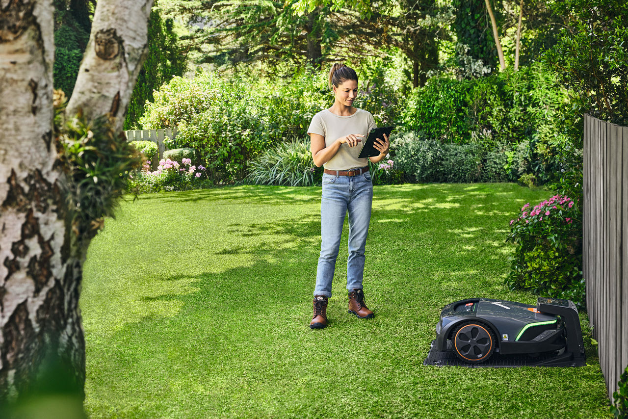 Una donna aziona lo STIHL iMOW® EVO tramite un tablet nel suo giardino