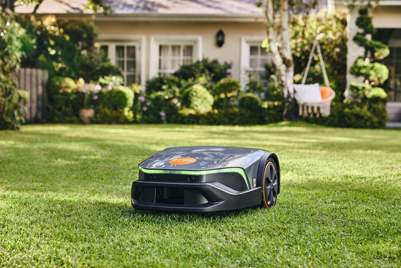 Un iMOW® EVO taglia il prato del giardino davanti a una casa